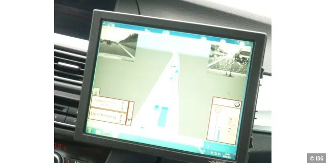 Der Kontrollbildschirm vor dem Beifahrerplatz. In den Ecken links und rechts oben sieht man die Bilder von der Front- und von der Heckkamera unseres Testwagens. In der Mitte des Bildschirms ist die Autobahn mit den Fahrzeugen darauf abgebildet. Und wir mitten drin.