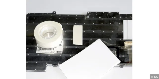 Mit einem Doppelklebeband werden auf der Unterseite der Tastatur zugeschnittene Pappstücke befestigt.