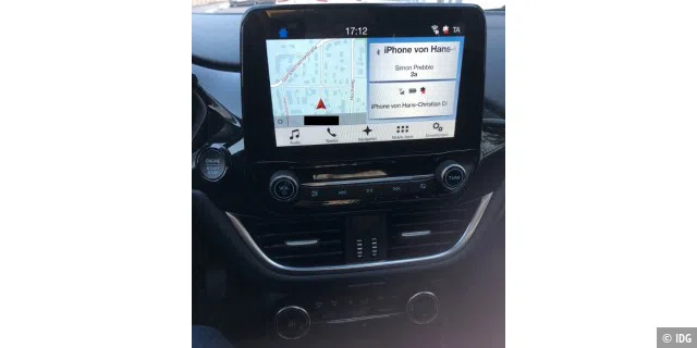 Der Touchscreen zeigt den Startbildschirm mit verkleinerter Navi-Karte, Unterhaltungsmenü und Telefonie. Darunter die diversen physischen Bedienelementen.